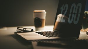 computer with 12:00 on the screen, a coffee cup and glasses